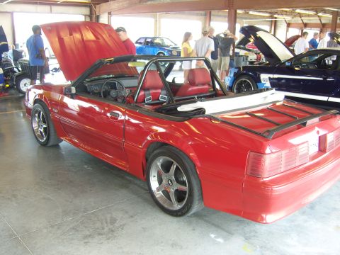 2007 Ford Mustang - A red convertible with a roll cage is parked indoors next to other vehicles.
