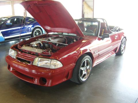 2007 Ford Mustang - Red convertible Mustang with hood open, engine visible. Another Mustang is parked behind it.