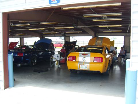 2007 Ford Mustang - Two Ford Mustangs, one yellow and one blue, are parked in a garage with hoods open.