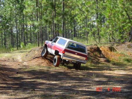 1991 Ford Bronco - A red and white SUV navigates a dirt path in a wooded area.