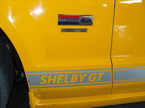 2007 Ford Mustang - Side view of a yellow 2007 Ford Mustang Shelby GT, showing its distinctive stripe and badges.