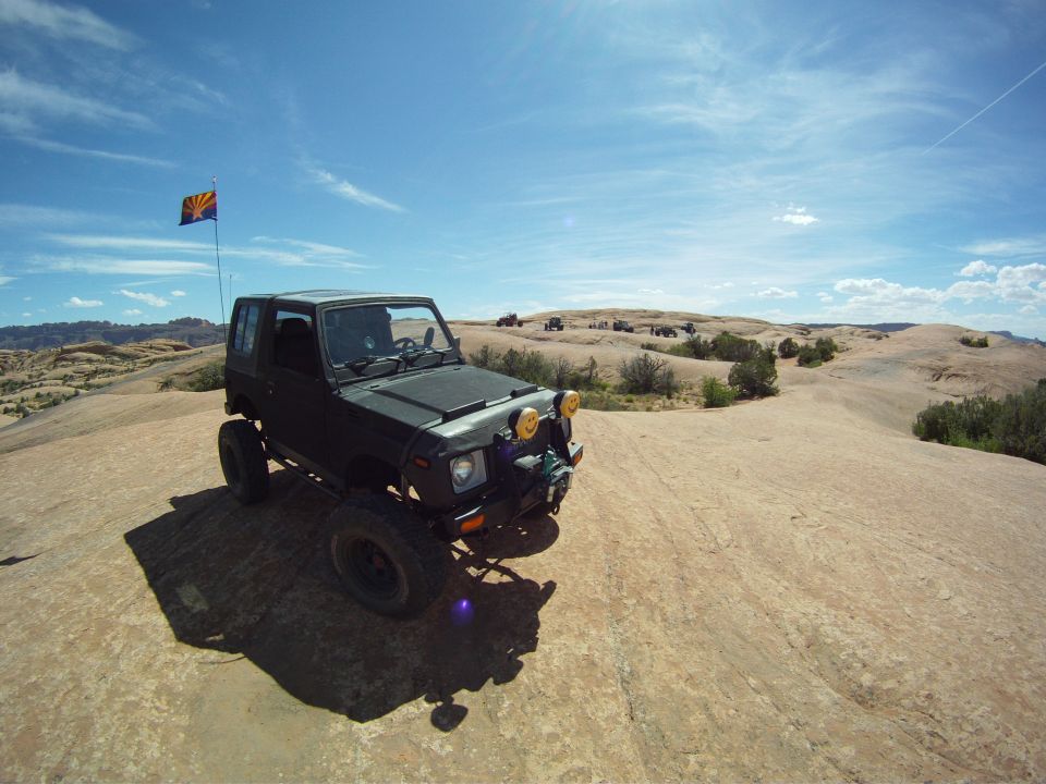 Lifted black Suzuki Samurai on slickrock with Arizona flag and yellow driving lights