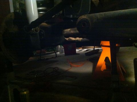 1990 Ford Bronco - The underside of a vehicle is visible, supported by orange jack stands in a dimly lit garage.