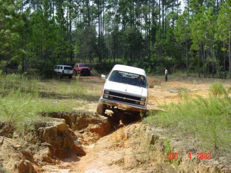 1991 Ford Bronco - White van attempts a challenging off-road obstacle with other vehicles present.