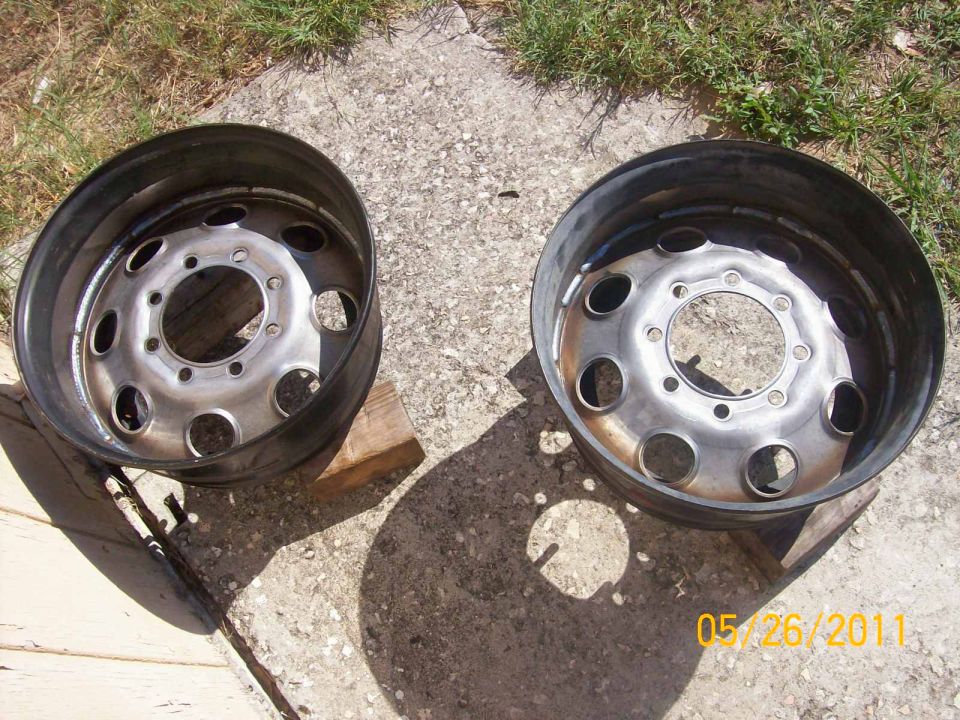 Two steel truck wheels with multiple lug holes sit on concrete