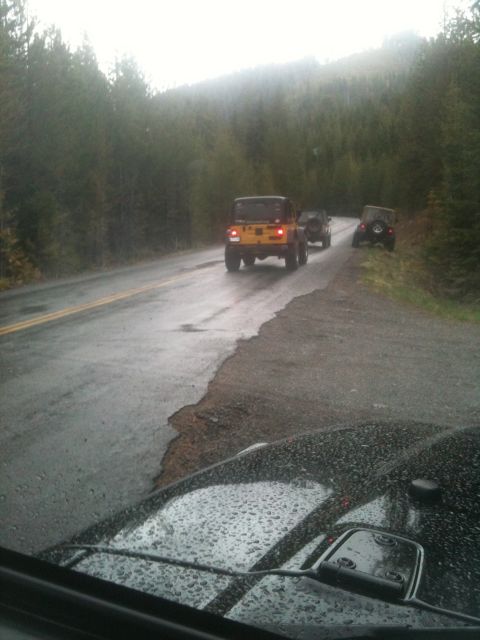 2005 Jeep Wrangler - A group of Jeeps travels down a rain-slicked road through a forest.