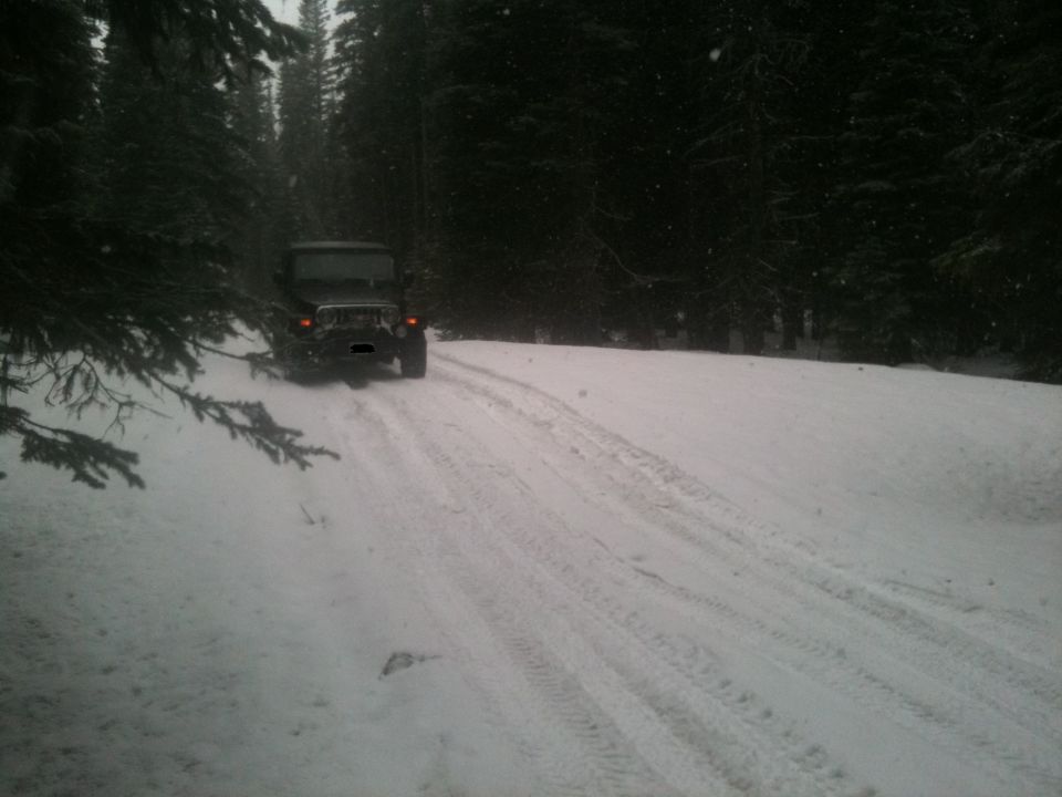 2005 Jeep Wrangler driving on a snow-covered dirt road through a forest