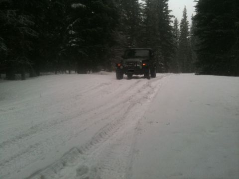 2005 Jeep Wrangler - A Jeep Wrangler navigates a snow-covered path surrounded by dark evergreen trees.