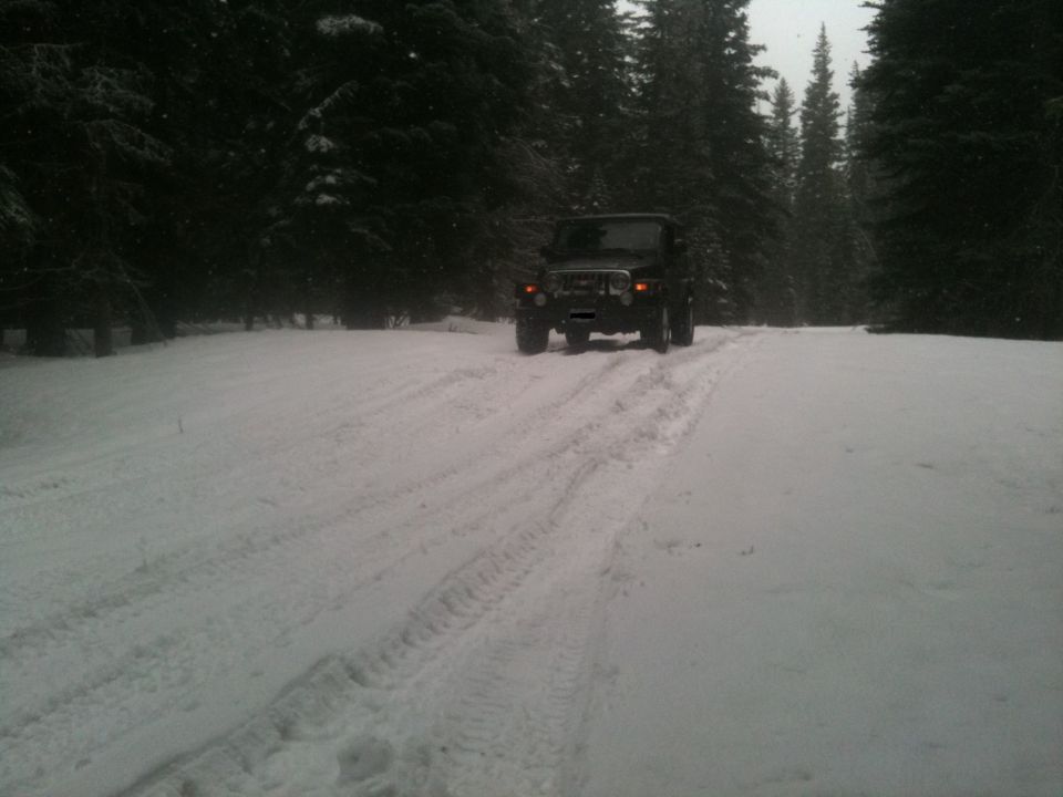 Jeep Wrangler driving on a snowy road through a forest