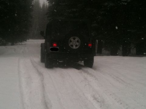 2005 Jeep Wrangler - A black Jeep Wrangler navigates a snow-covered road surrounded by trees.