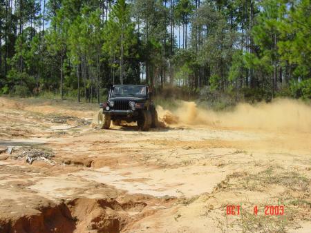 1991 Ford Bronco - A Jeep Wrangler navigates a dusty off-road trail, sending a plume of dirt into the air.