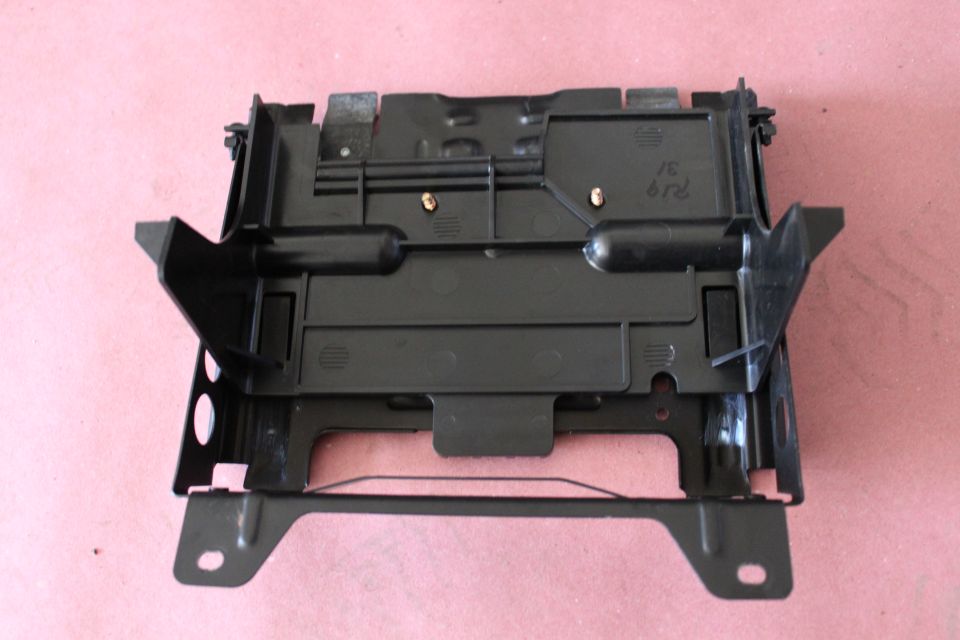 Black automotive plastic and metal bracket assembly on pink background with handwritten markings
