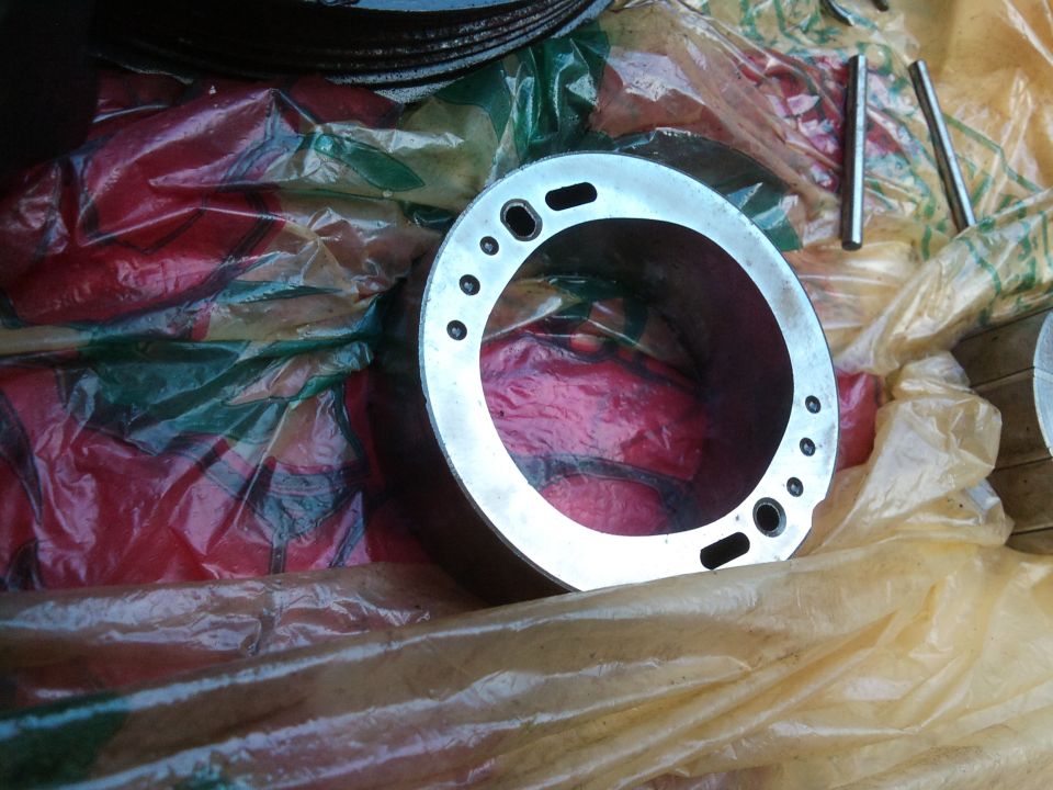 Metal cylinder part with multiple holes around its circumference, resting on plastic sheeting