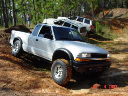 1991 Ford Bronco - A white pickup truck navigates a challenging off-road course with other vehicles in the background.