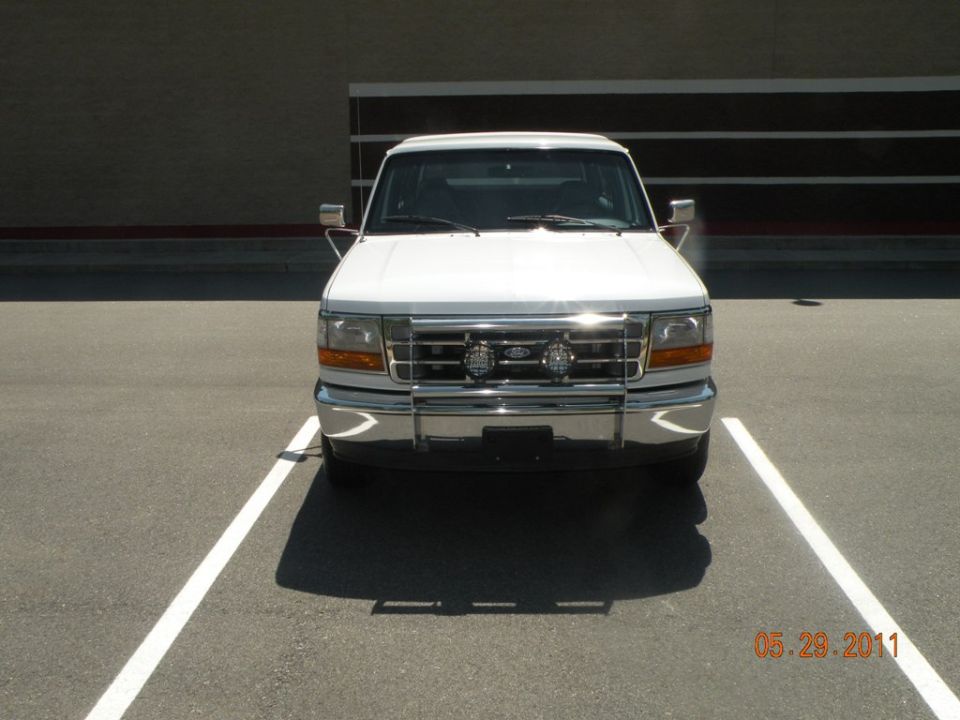 White Ford truck parked in a lot, front view. Has a chrome bumper and grille