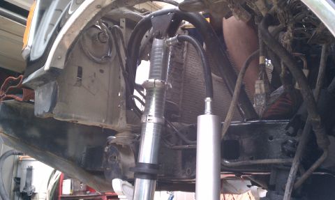 1990 Ford Bronco - Close-up view of a modified front suspension system, showing hydraulic lines and a shock absorber assembly.