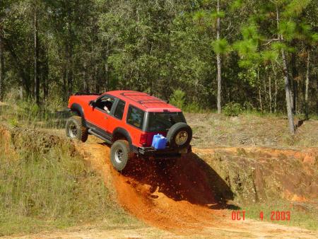 1991 Ford Bronco - Red SUV navigates a steep dirt hill during off-road activity.