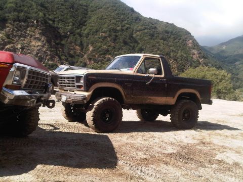 1986 Ford Bronco - This lifted 1980s Ford Bronco is seen in a mountainous area, parked alongside another vehicle.