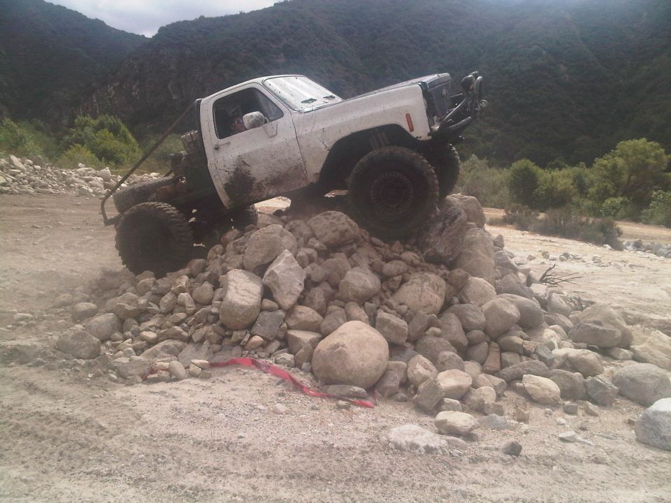 White pickup truck with off-road modifications climbing over a pile of rocks