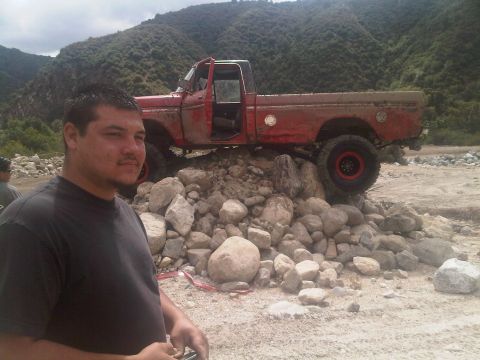 1986 Ford Bronco - A man stands in front of a red pickup truck that is positioned on a rocky incline in a natural setting.