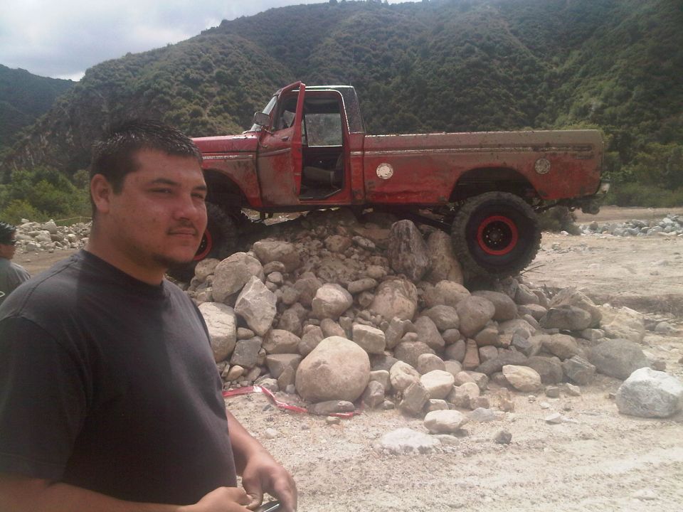 Man in foreground, red pickup truck with open door perched on a pile of rocks
