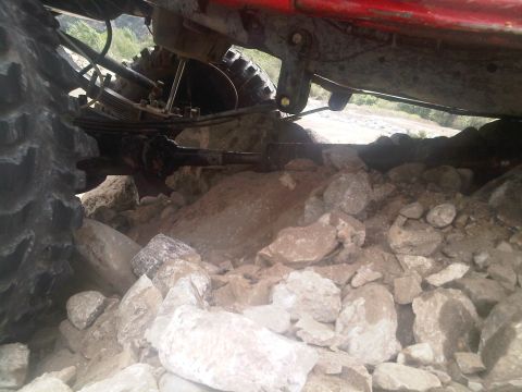 1986 Ford Bronco - The undercarriage of a red vehicle is visible, with large tires partially submerged in rocks.