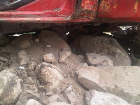 1986 Ford Bronco - A red vehicle appears to be stuck on a pile of rocks, with its undercarriage clearly visible.