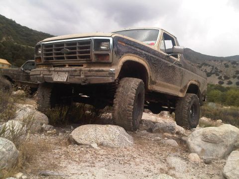 1986 Ford Bronco - A lifted Ford Bronco navigates a rocky trail, with another vehicle visible in the background.