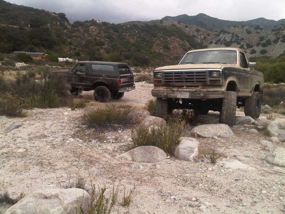 Tan 1980s Ford F-Series truck and dark Bronco off-road