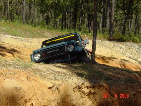 1991 Ford Bronco - A Suzuki Samurai is stuck on a dirt embankment with a tree nearby.