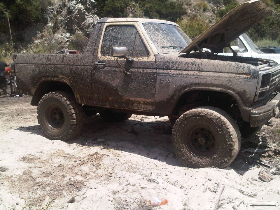 Muddy SUV with hood up, parked on dirt. Another vehicle is partially visible behind it