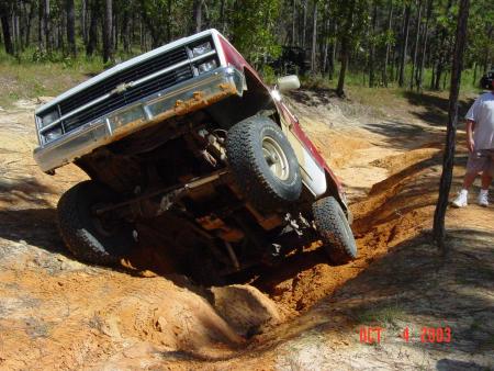 1991 Ford Bronco - A red and white pickup truck is tilted on its side while navigating a challenging off-road trail.