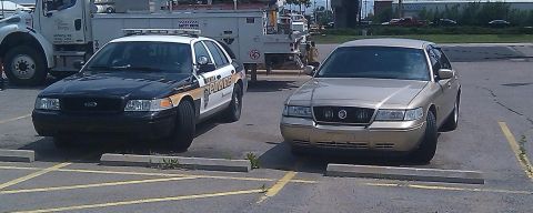 2000 Mercury Grand Marquis - Two sedans, a gold Mercury Grand Marquis and a police car, are parked in a lot.