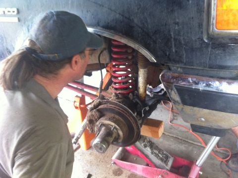 1990 Ford Bronco - A mechanic works on the suspension of a lifted vehicle, focusing on the front wheel assembly and coilover.