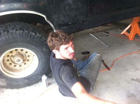 1990 Ford Bronco - Man works on a 1990 Ford Bronco that is lifted on an orange jack stand.