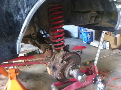 1990 Ford Bronco - Close-up of a vehicle's front wheel hub, brake rotor, and suspension components, supported by jack stands.