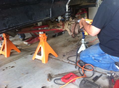 1990 Ford Bronco - A person is working on the suspension of a vehicle that is raised on jack stands.