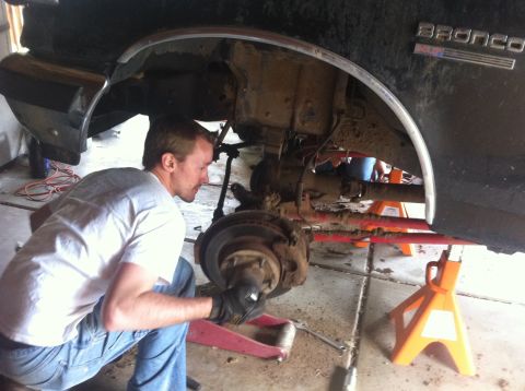 1990 Ford Bronco - A mechanic works on the suspension of a Ford Bronco that is raised on jack stands.