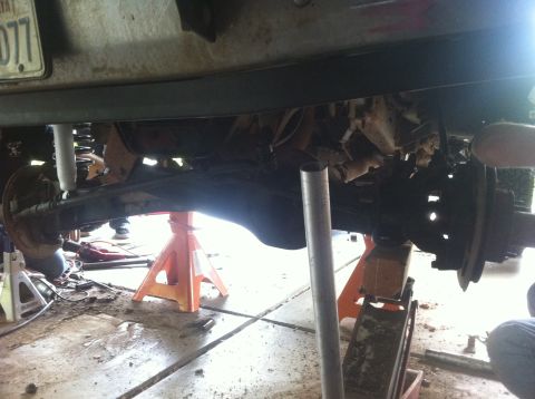 1990 Ford Bronco - A vehicle's undercarriage is inspected while elevated on jack stands in a workshop.