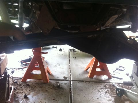 1990 Ford Bronco - The underside of a vehicle is elevated on orange jack stands, revealing its suspension and drivetrain parts.