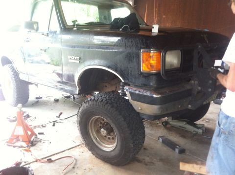 1990 Ford Bronco - Black Ford Bronco with lifted suspension and large tires is shown from the front-right angle in a garage.