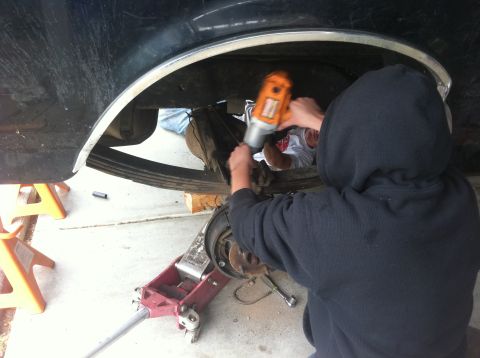1990 Ford Bronco - Mechanics work on the rear suspension of a 1990 Ford Bronco, lifted on jack stands.