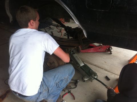 1990 Ford Bronco - A person is working on the underside of a vehicle, which is supported by jacks.