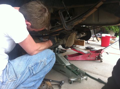 1990 Ford Bronco - A person is working on the rear axle of a vehicle that is supported by two floor jacks.