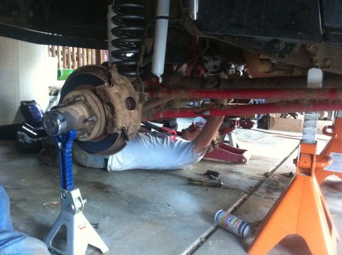1990 Ford Bronco - A person works on the undercarriage of a vehicle, focusing on the suspension and brake components.