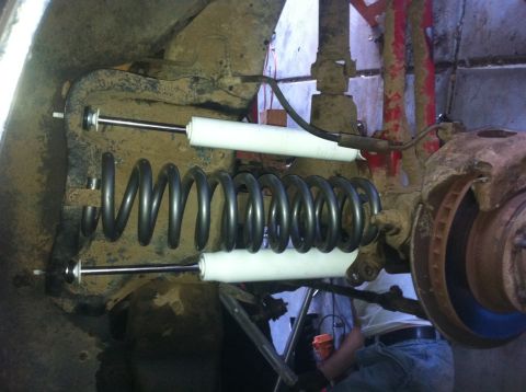 1990 Ford Bronco - Close-up view of vehicle suspension parts, including a large coil spring and white shock absorbers.