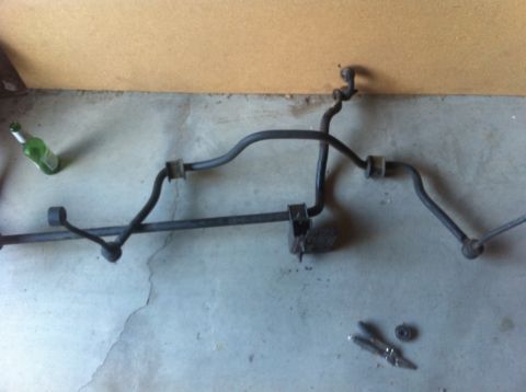 1990 Ford Bronco - An anti-roll bar assembly is shown on a concrete floor, with a green bottle and hardware nearby.