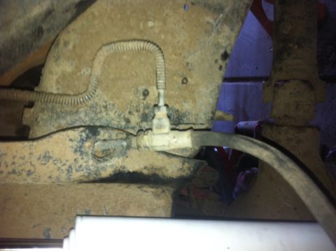 1990 Ford Bronco - Undercarriage view shows a brake line assembly with visible dirt and grime on the suspension parts.