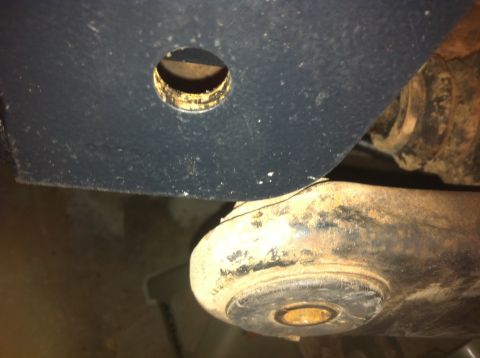 1990 Ford Bronco - Detail of a rusty suspension part, showing wear and a bolt hole, from a vehicle's undercarriage.