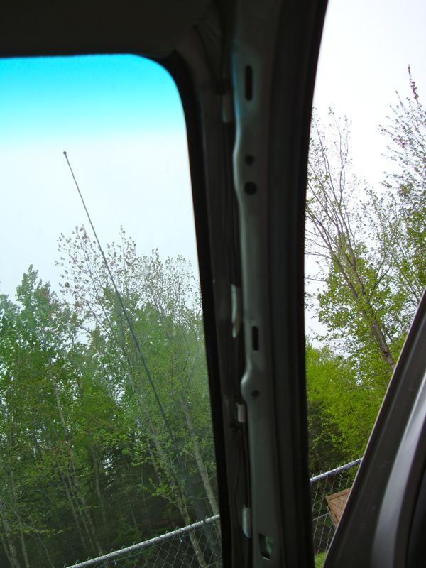 Interior pillar with visible mounting holes and a long antenna extending upwards against a backdrop of trees